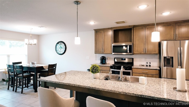 kitchen featuring decorative light fixtures, appliances with stainless steel finishes, a sink, a notable chandelier, and a breakfast bar