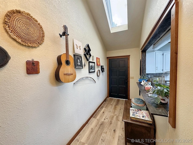 doorway to outside featuring light wood finished floors, a textured wall, and a skylight