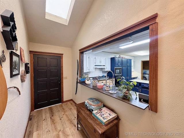 interior space with visible vents, light wood finished floors, lofted ceiling with skylight, and a textured wall
