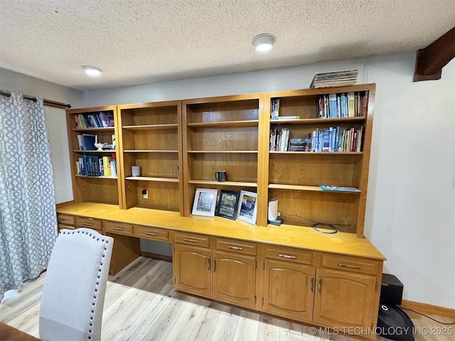 office area with light wood-style floors, a textured ceiling, and built in desk