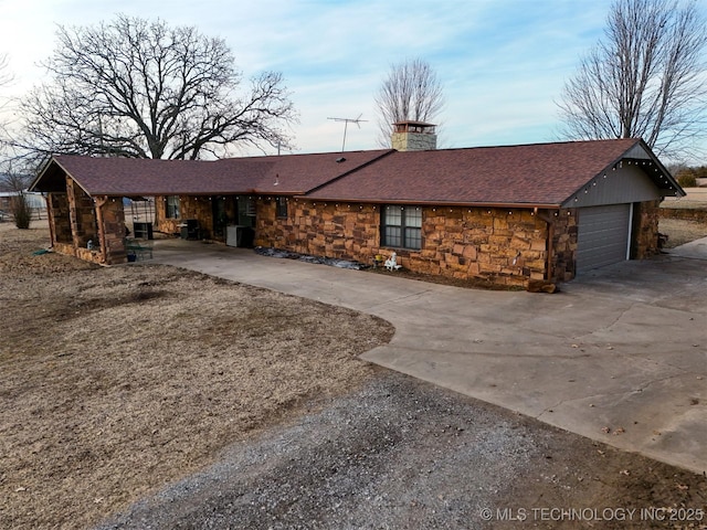 view of front of property with a shingled roof, an attached garage, stone siding, a chimney, and driveway