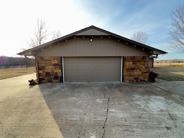view of side of home featuring fence, an outbuilding, stone siding, and a detached garage