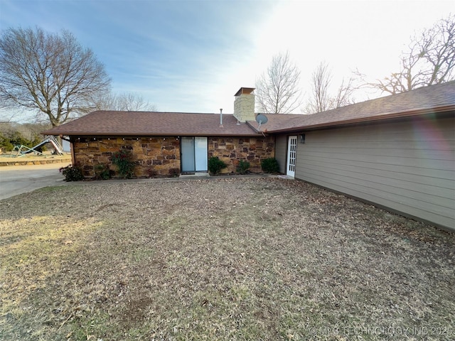 back of house featuring a chimney and stone siding