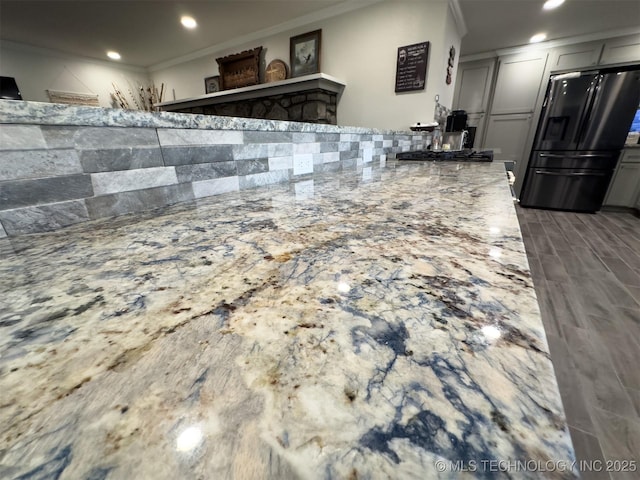 kitchen with crown molding, recessed lighting, black refrigerator with ice dispenser, and light stone counters