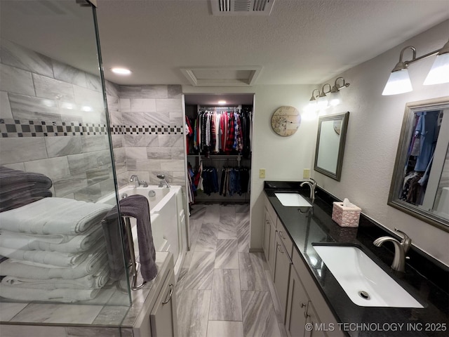 bathroom featuring a walk in closet, visible vents, a sink, and a garden tub