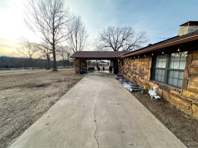 exterior space featuring concrete driveway, fence, and stone siding
