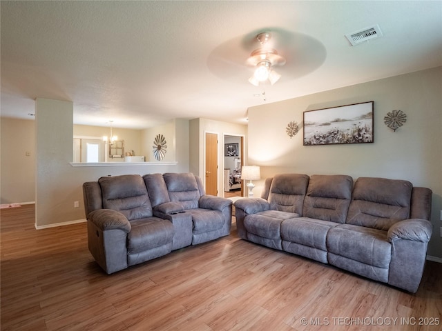 living area with visible vents, light wood finished floors, and ceiling fan with notable chandelier