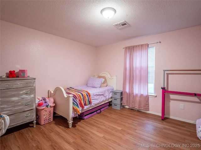 bedroom with visible vents, a textured ceiling, baseboards, and wood finished floors