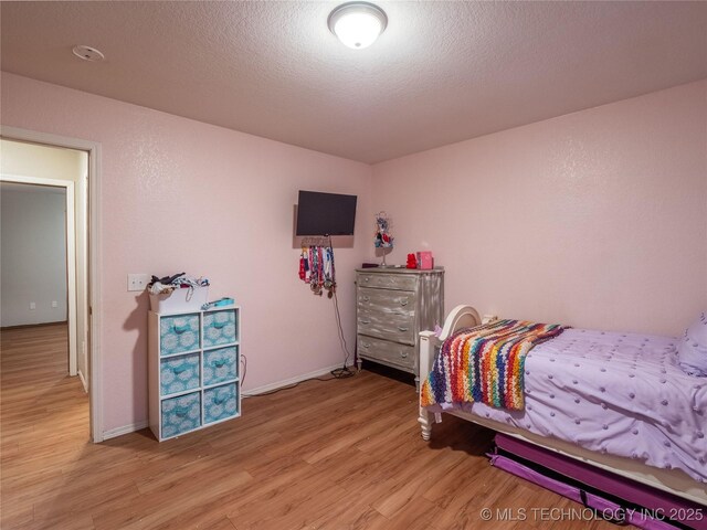 bedroom featuring light wood-type flooring, a textured ceiling, and baseboards