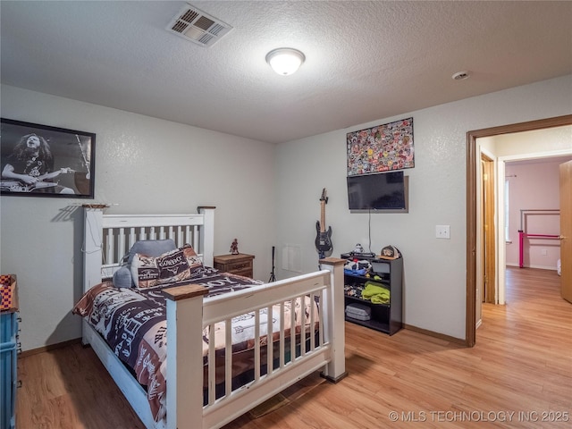 bedroom featuring visible vents, baseboards, a textured ceiling, and wood finished floors