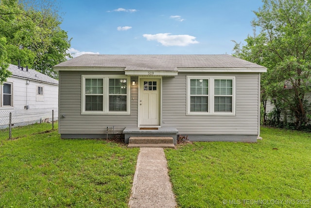 bungalow-style house with fence, a shingled roof, and a front lawn