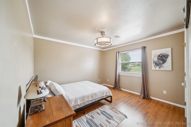 bedroom with baseboards, ornamental molding, visible vents, and light wood-type flooring