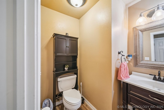 half bath with vanity, baseboards, toilet, and wood finished floors
