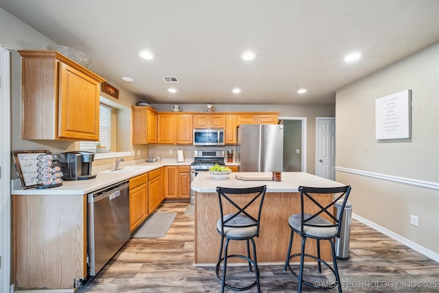 kitchen with appliances with stainless steel finishes, light wood-style floors, light countertops, a kitchen island, and visible vents