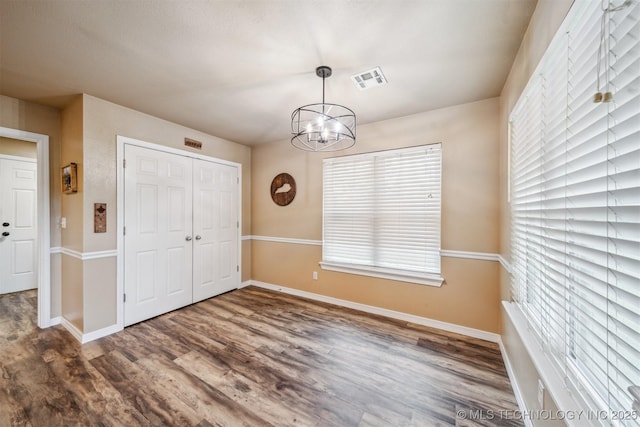 unfurnished dining area featuring baseboards, wood finished floors, a notable chandelier, and visible vents