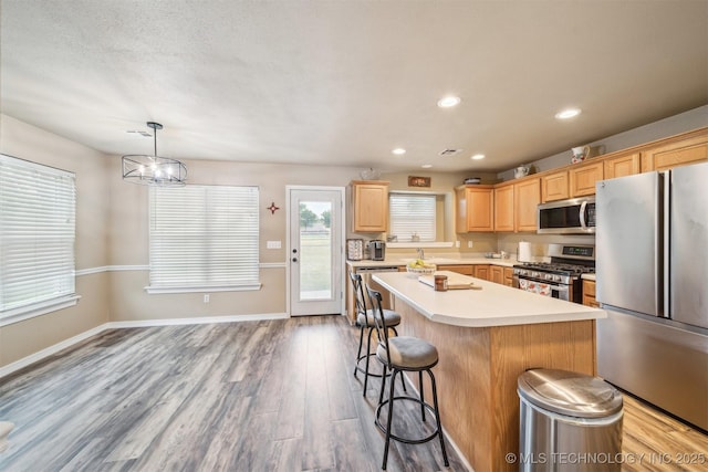 kitchen with appliances with stainless steel finishes, light brown cabinets, light countertops, a kitchen bar, and a kitchen island