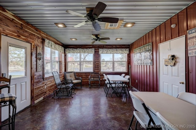 interior space with wooden walls, a ceiling fan, finished concrete floors, and visible vents