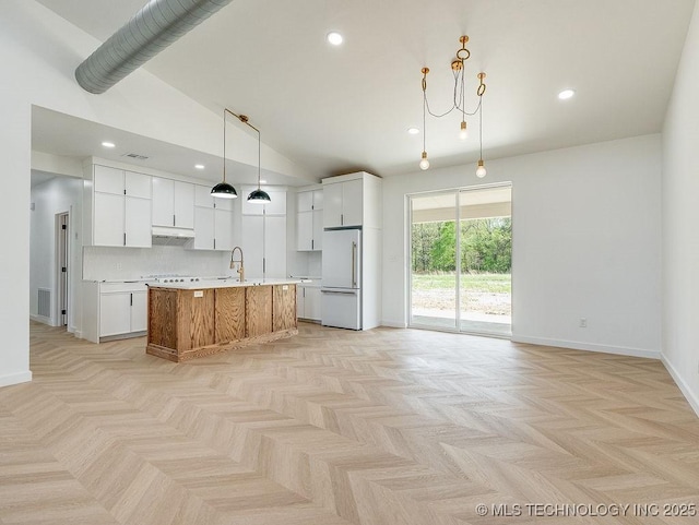 kitchen with high end white fridge, light countertops, white cabinetry, and an island with sink