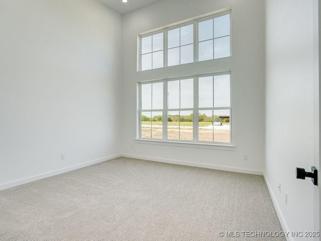 empty room with carpet floors, baseboards, and a high ceiling