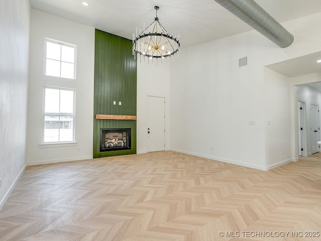 unfurnished living room with visible vents, a towering ceiling, a chandelier, and a wealth of natural light