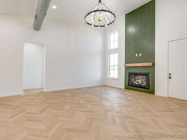 unfurnished living room with a high ceiling, a chandelier, a large fireplace, and baseboards