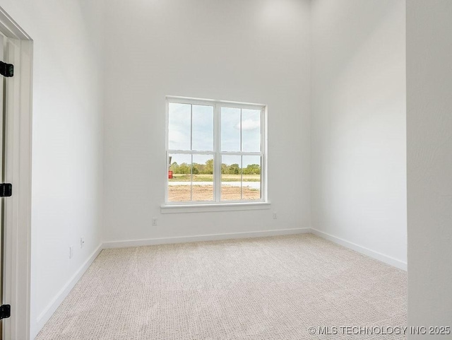 unfurnished room with carpet floors, baseboards, and a high ceiling