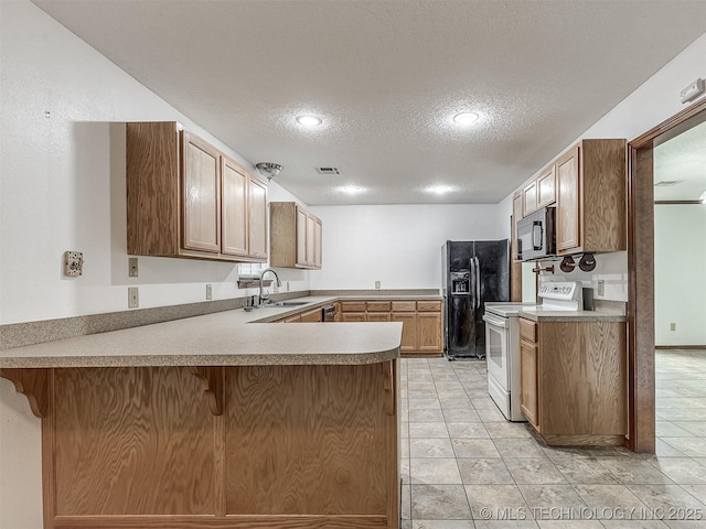 kitchen featuring visible vents, a peninsula, a textured ceiling, a sink, and black appliances