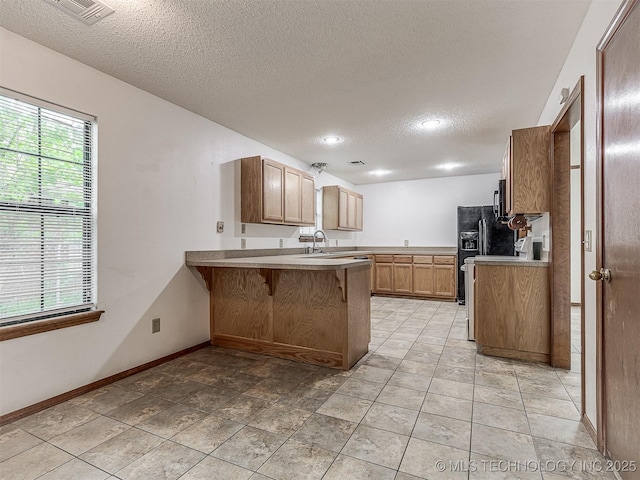 kitchen with visible vents, a peninsula, a kitchen breakfast bar, a textured ceiling, and a sink