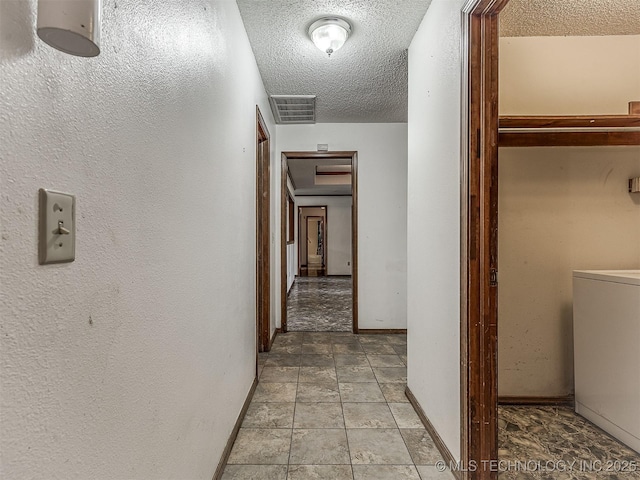 corridor with visible vents, a textured ceiling, baseboards, and washer / dryer