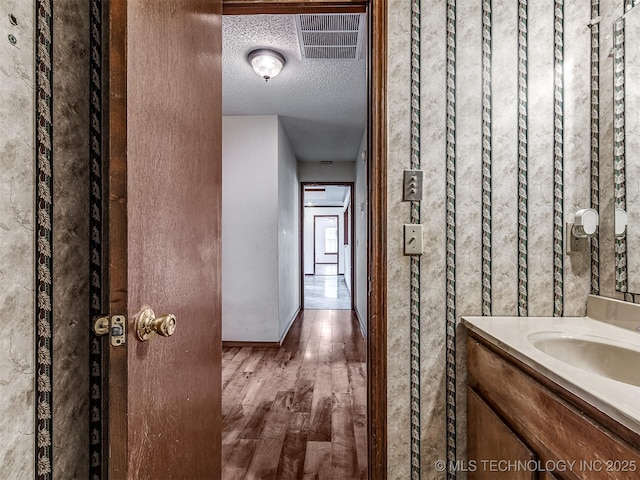 hallway featuring visible vents, wood finished floors, baseboards, a textured ceiling, and a sink
