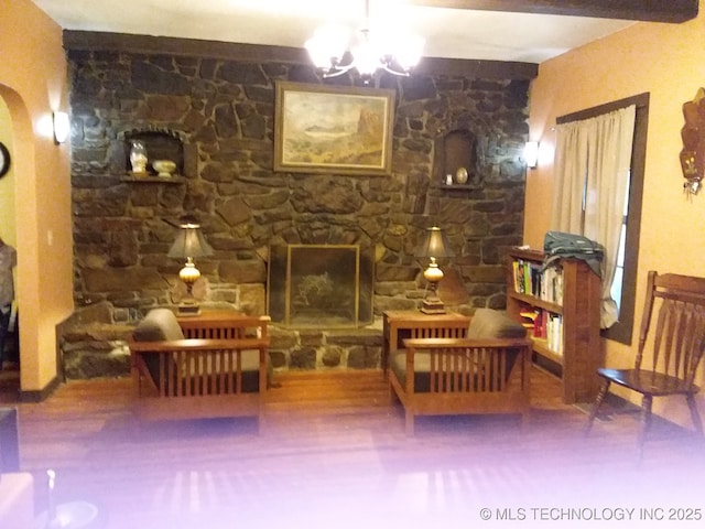 living area with wood finished floors, a stone fireplace, and a notable chandelier