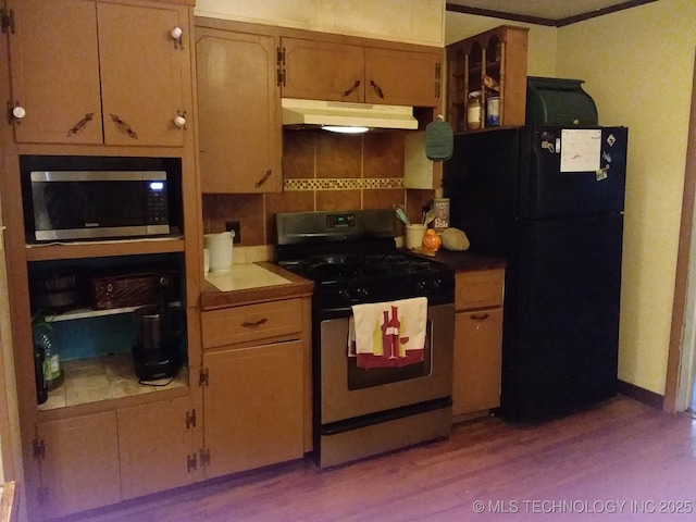 kitchen featuring tasteful backsplash, wood finished floors, under cabinet range hood, ornamental molding, and stainless steel appliances