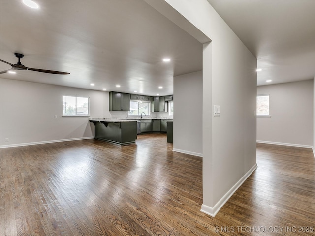 unfurnished living room with a healthy amount of sunlight, baseboards, a ceiling fan, and dark wood-type flooring