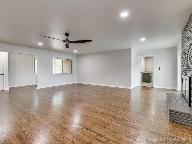 unfurnished living room featuring ceiling fan, a brick fireplace, wood finished floors, baseboards, and recessed lighting
