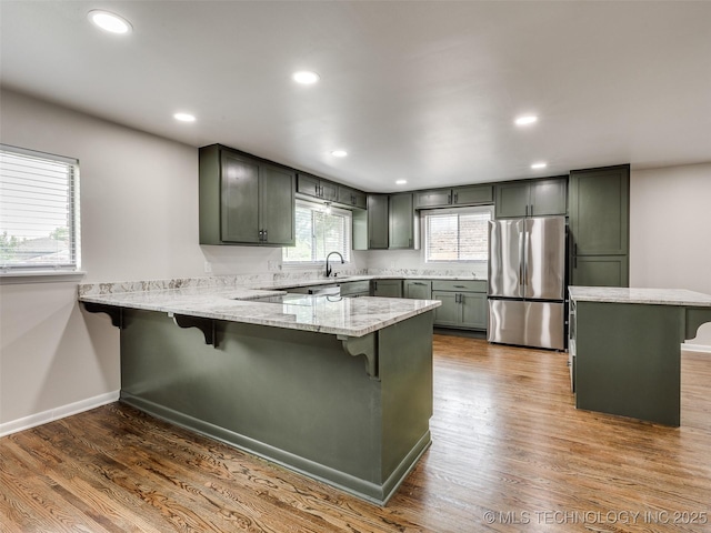 kitchen with a kitchen bar, light stone counters, freestanding refrigerator, a peninsula, and green cabinetry
