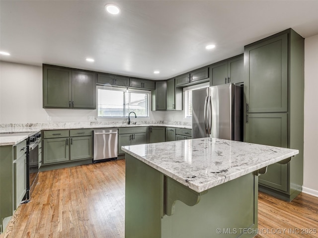 kitchen featuring a kitchen bar, appliances with stainless steel finishes, light stone countertops, green cabinetry, and light wood-style flooring