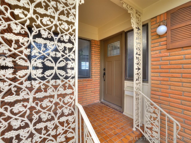 view of exterior entry with brick siding and a porch