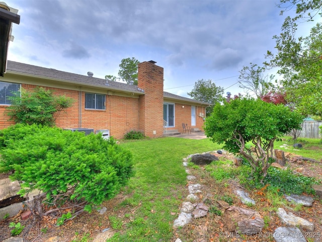 back of house featuring fence, a patio, a chimney, brick siding, and a lawn