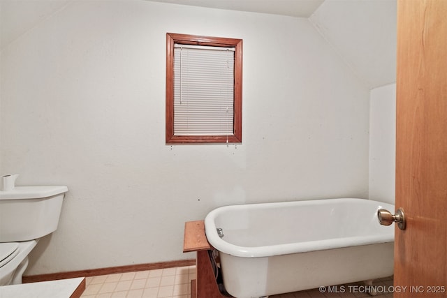 bathroom with baseboards, vaulted ceiling, toilet, and a soaking tub
