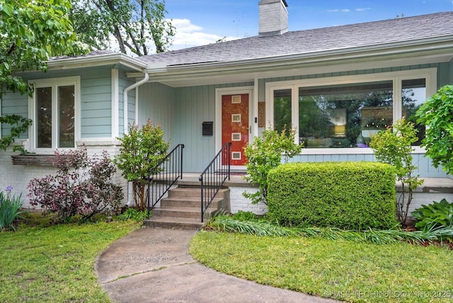 entrance to property featuring a shingled roof, a chimney, and a yard