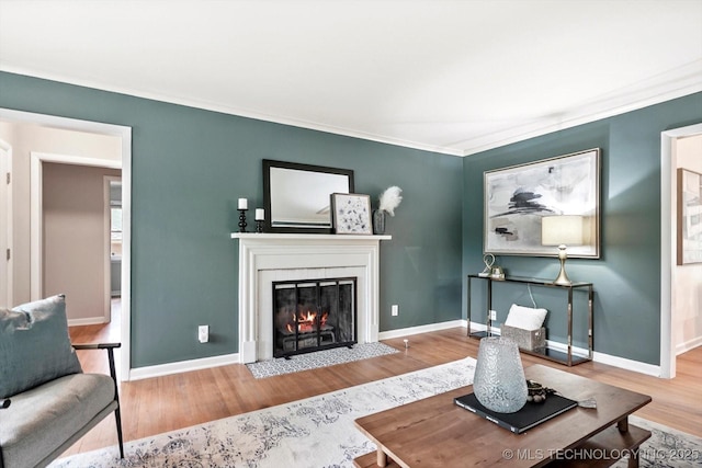 living area with a fireplace with flush hearth, baseboards, ornamental molding, and wood finished floors