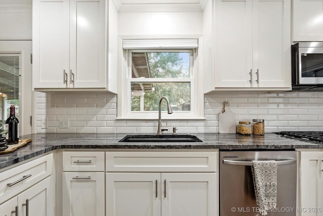 kitchen featuring dark stone counters, white cabinets, a sink, appliances with stainless steel finishes, and backsplash