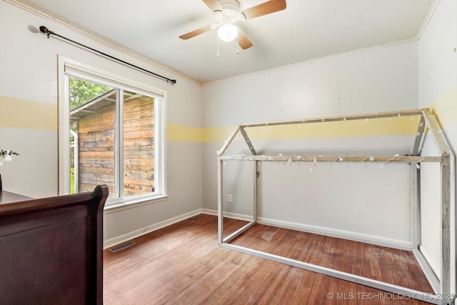 unfurnished bedroom featuring a ceiling fan, visible vents, crown molding, wood finished floors, and baseboards