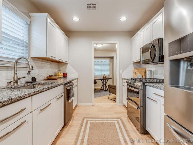 kitchen with appliances with stainless steel finishes, a sink, baseboards, tasteful backsplash, and visible vents