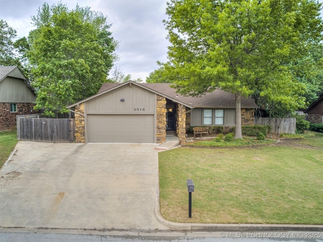 mid-century home featuring fence, a front yard, stone siding, an attached garage, and driveway