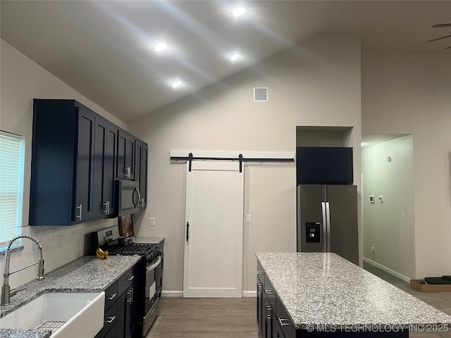 5114 W 3rd St, Tulsa, OK 74127 - kitchen featuring vaulted ceiling, a barn door, a sink, light stone counters, and stainless steel appliances