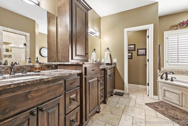 bathroom featuring vanity, stone tile floors, baseboards, and a bath
