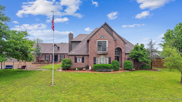 tudor home with brick siding, a front lawn, fence, and a chimney