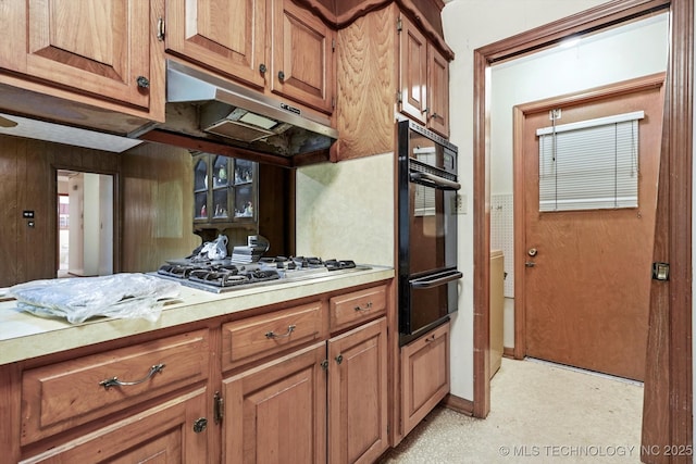 kitchen with light countertops, black oven, brown cabinetry, under cabinet range hood, and a warming drawer