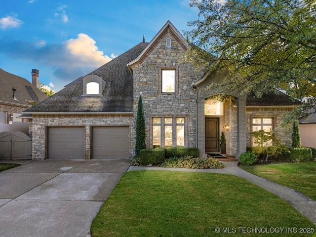 french country home featuring stone siding, a front yard, a gate, an attached garage, and driveway